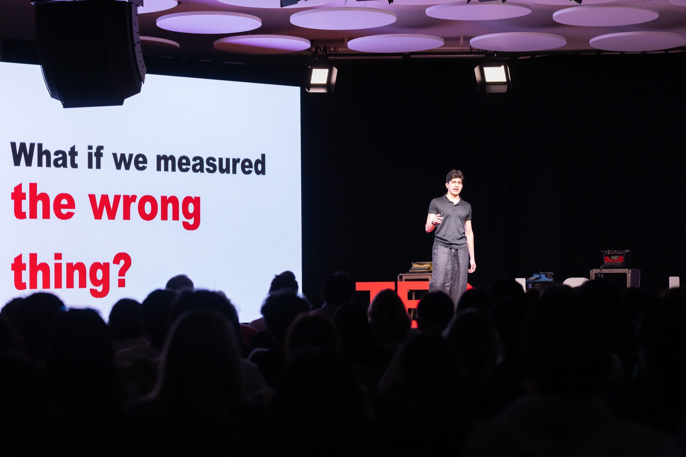 Mo Shirmohammadi delivering a TEDx talk at La Sierra University, on stage beside the slide reading 'What if we measured the wrong thing?'